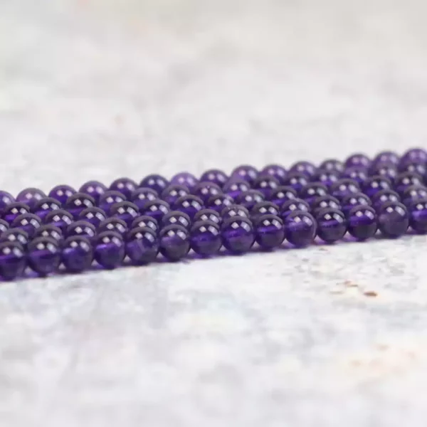 plusieurs brins de perles d'améthyste ronde de 4mm disposées en long sur une table. la couleur violette est profonde et les perles sont sans défaut